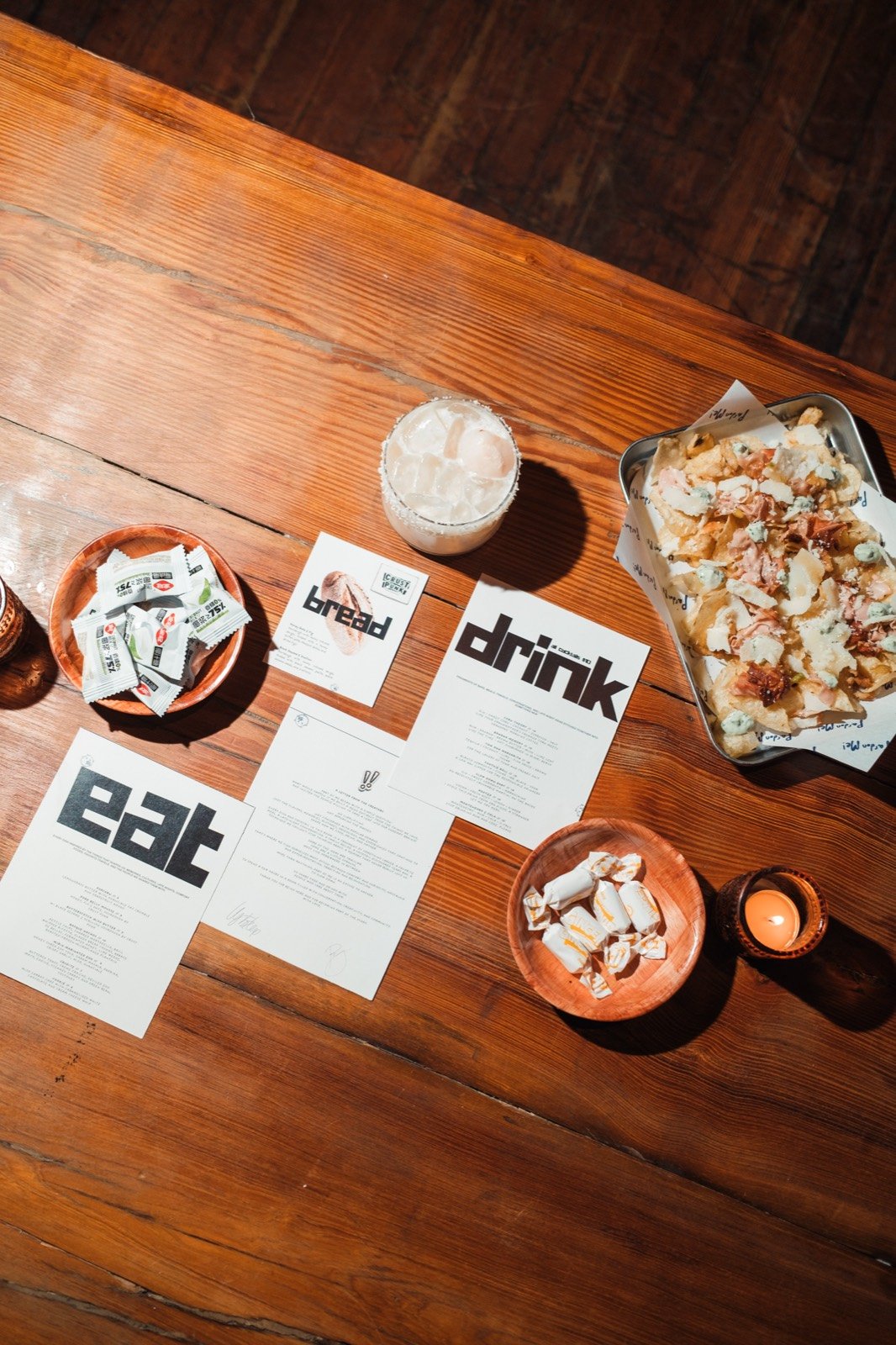 Printed eat, drink, and bread menus laid out on a wood table with plates from vol. 1